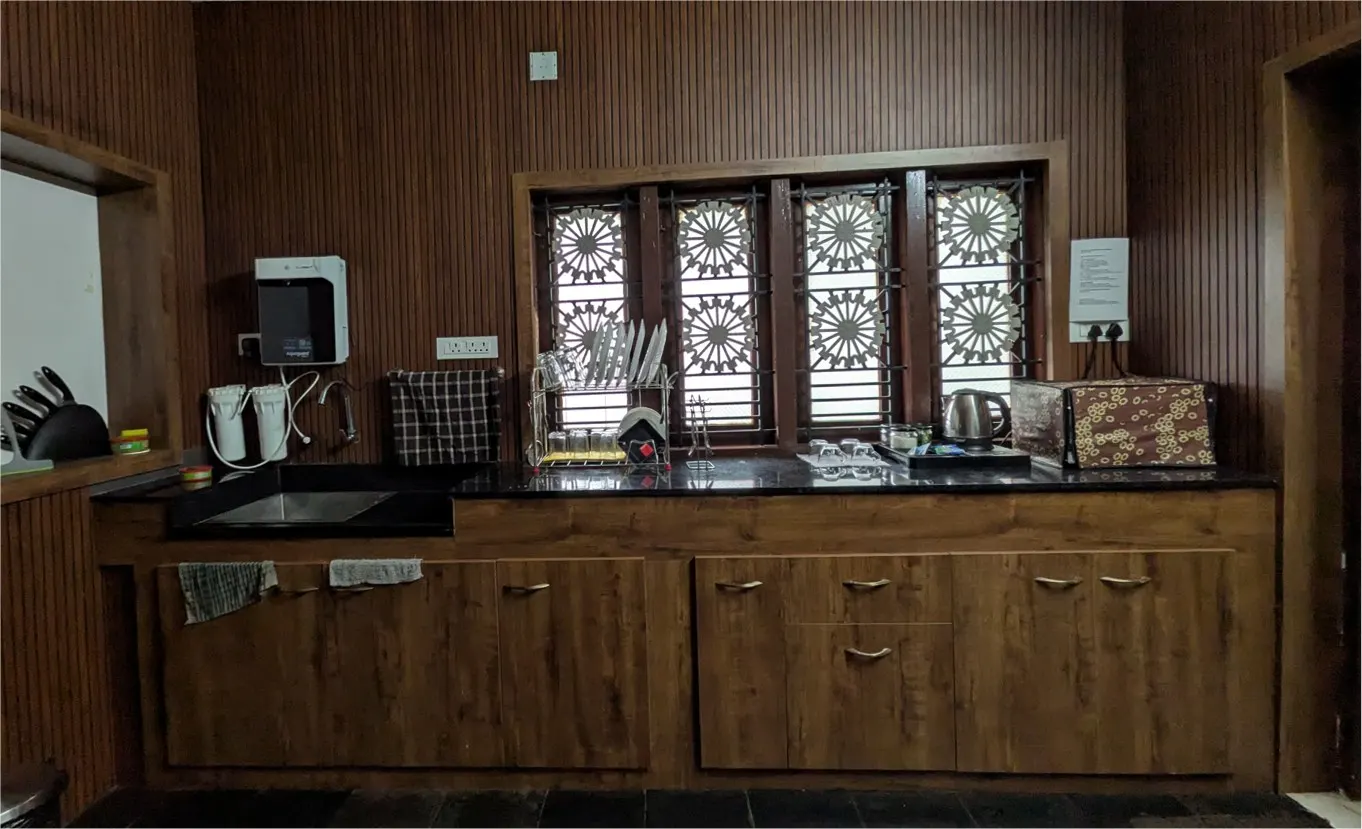 The fully equipped private kitchen at Riverside Retreat featuring dark wood cabinets, traditional latticework windows, a granite countertop, and an Aquaguard water purifier.