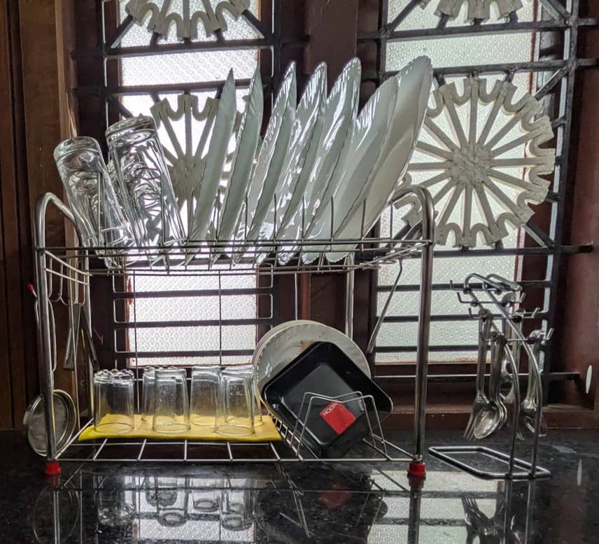 A stainless steel dish drying rack filled with clean white plates, glassware, and cookware on a granite counter in the Riverside Retreat kitchen.